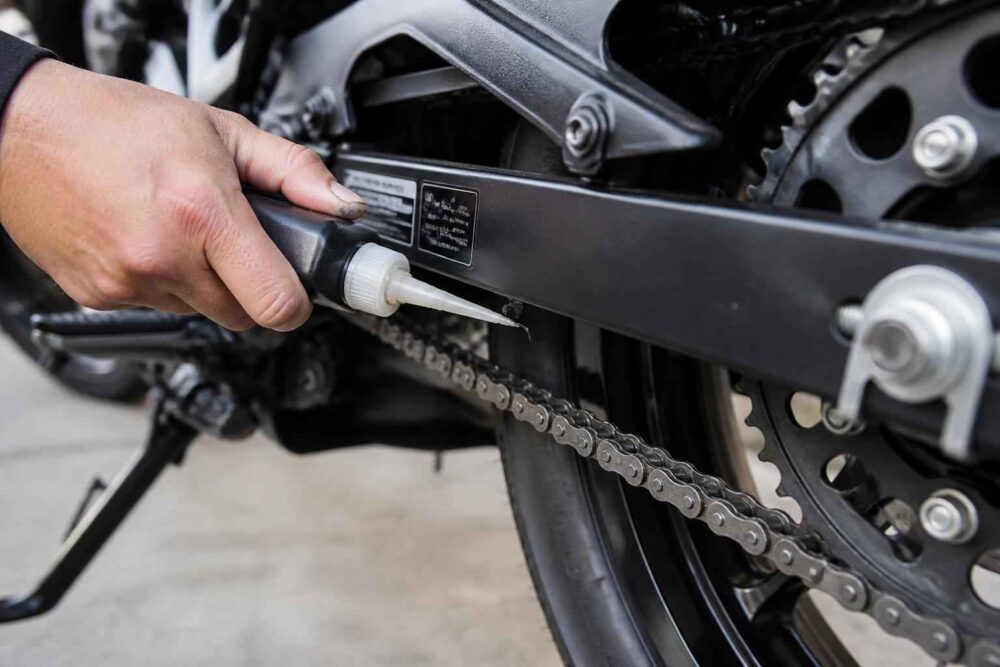 Dłoń nanosi preparat na łańcuch motocykla przy użyciu małego aplikatora