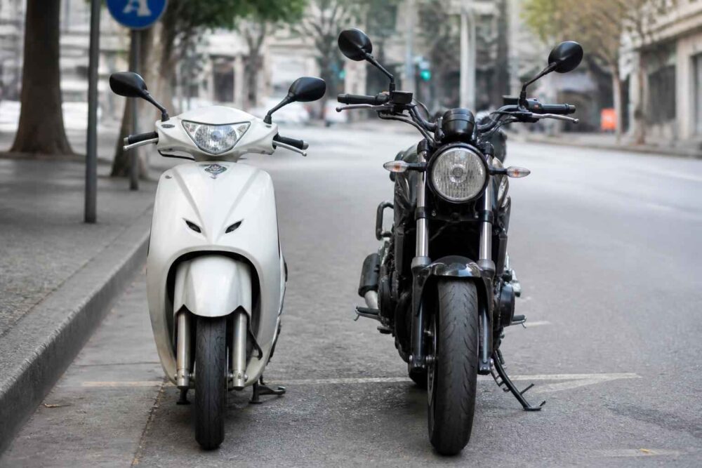 Biały skuter i czarny motocykl ustawione na ulicy Biały skuter stoi obok czarnego motocykla na miejskiej ulicy