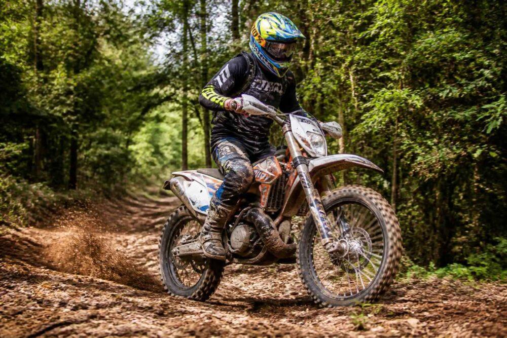 Motocyklista w kasku jedzie motocyklem enduro leśną ścieżką wśród drzew