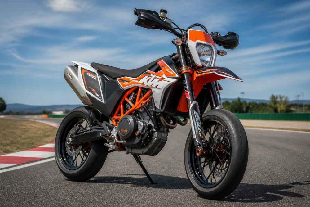 Pomarańczowy motocykl KTM zaparkowany na asfaltowym torze wyścigowym pod błękitnym niebem