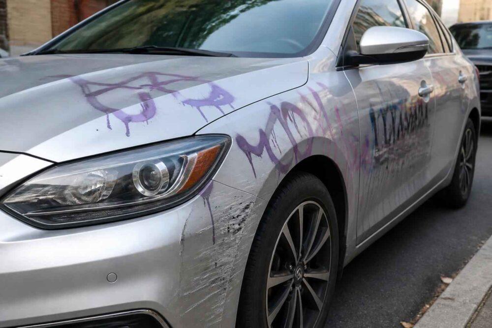 Srebrny samochód z fioletowym graffiti na masce i drzwiach oraz otarciami przy przednim kole